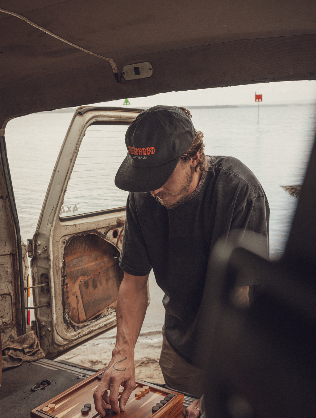 Man in a Boofhead Australia cap playing backgammon inside a vehicle